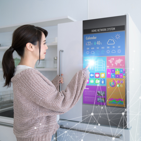 Shows a woman using an Internet of Things enabled refrigerator featuring weather, calendar, and other smart home features.
