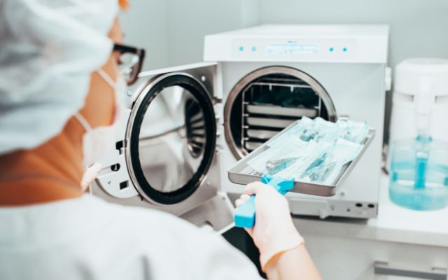A nurse loads a surgical tray into autoclave for sterilization