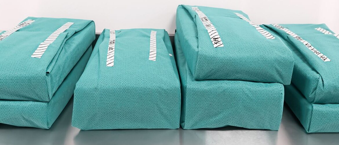 Shows stacks of sterilized and wrapped surgical trays on shelf