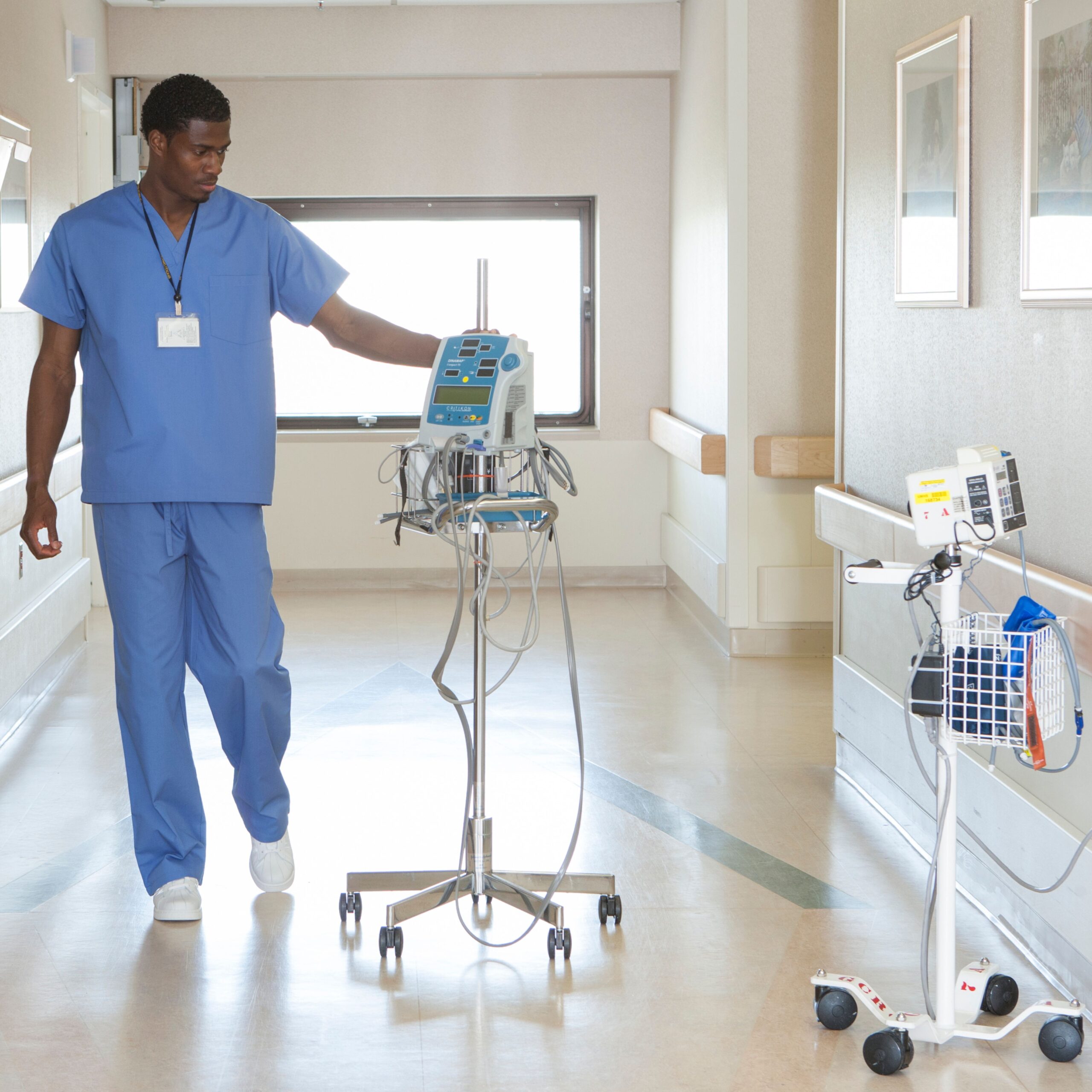 Shows a male nurse transporting an infusion pump in a hospital hallway